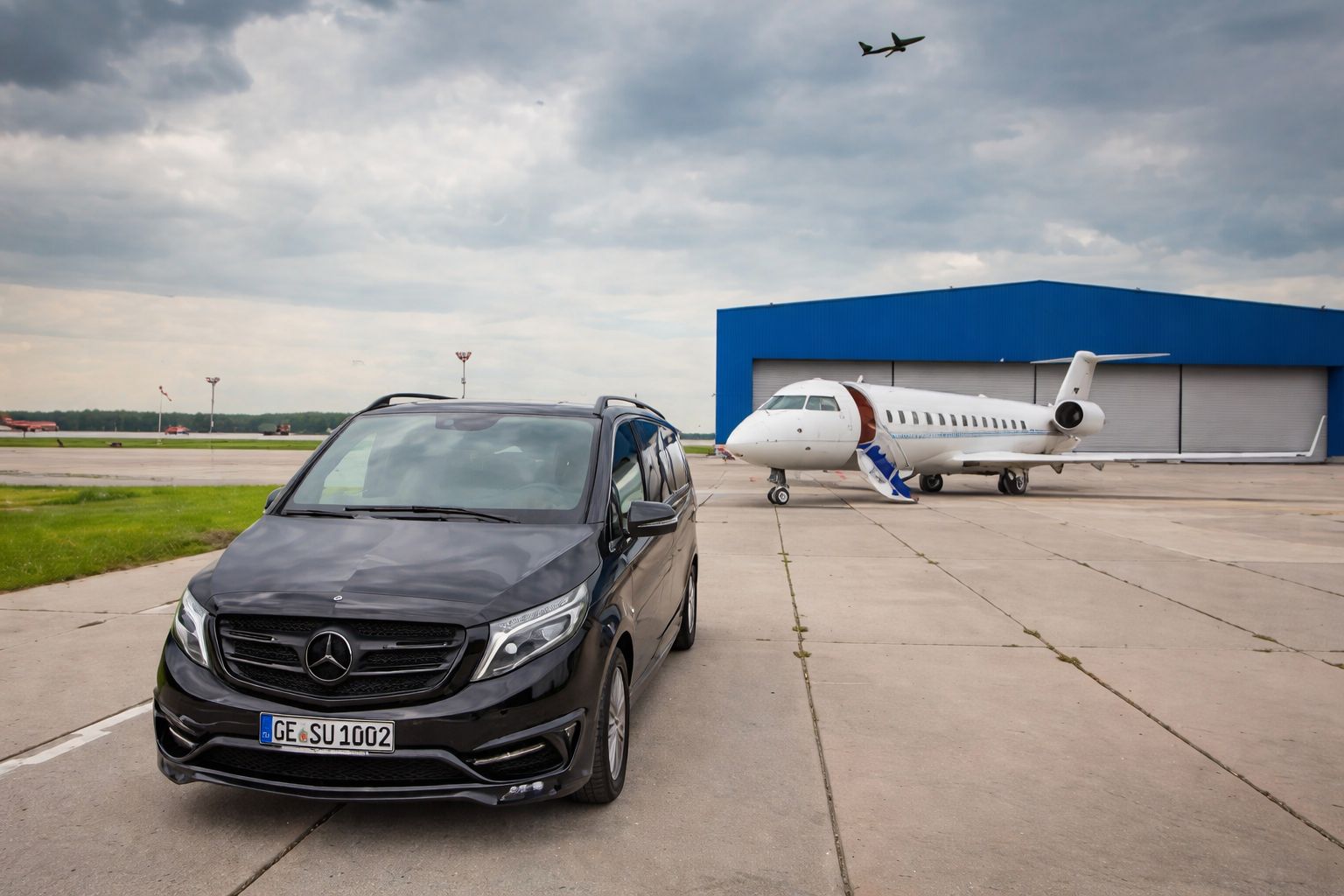 Ein schwarzer Mercedes Van steht auf dem Flugfeld vor einem weißen Privatjet und Hangar