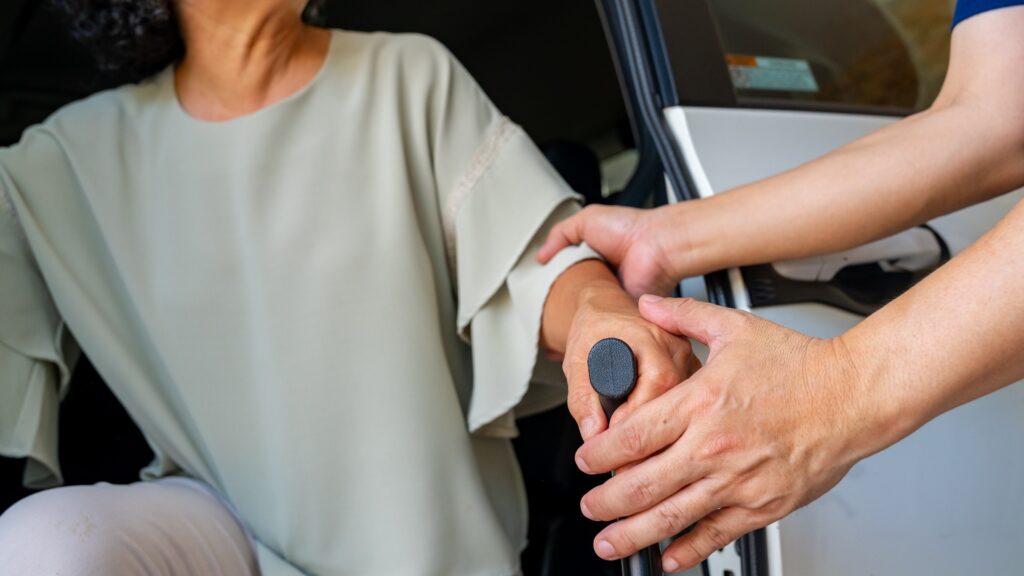 Ein asiatischer Pfleger oder Taxifahrer hilft einer älteren Patientin beim Einsteigen ins Auto, um sie zu Arztterminen oder Therapiesitzungen im Krankenhaus zu bringen. Fahrdienst für ältere Patienten.