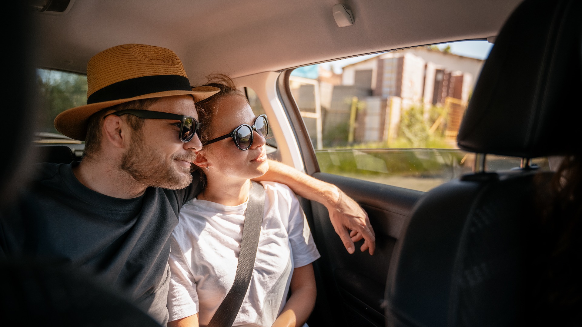 Ein junges, fröhliches Reisepaar sitzt auf dem Rücksitz eines Autos und schaut aus dem Fenster