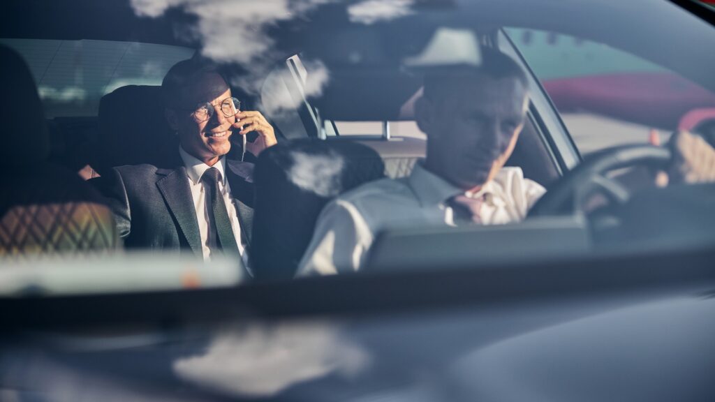 Ein lächelnder Geschäftsmann mit Smartphone, der mit Chauffeur unterwegs ist