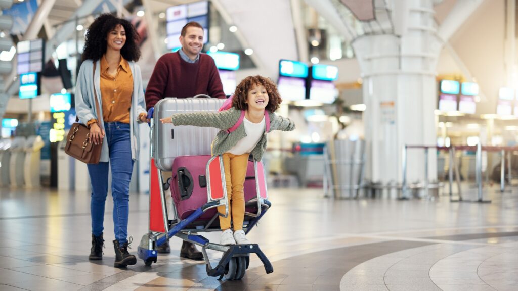 Flughafen, Familie und Kind freuen sich auf den Flug mit einem Koffertrolley – sei es im Urlaub, auf einer Reise oder bei der Einwanderung. Gepäck von Mutter, Vater oder Eltern unterschiedlicher Herkunft mit einem kleinen Mädchen in der Abflughalle